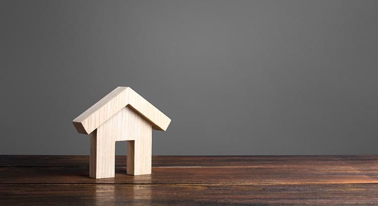 A small, minimalist wooden house model rests on a dark wooden surface, showcasing clean lines and natural textures.