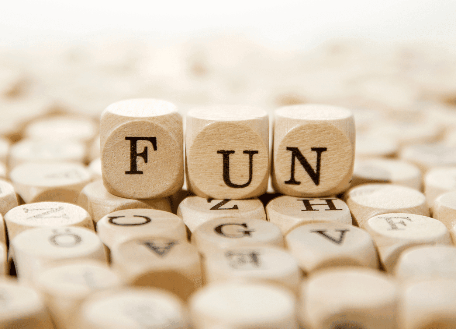 Three wooden letter dice spell out FUN and are surrounded by many other playful lettered dice scattered around.