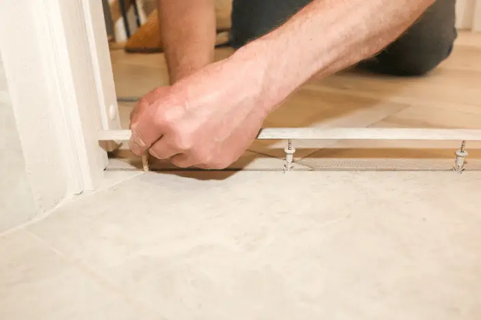 A person installs a metal transition strip between two types of flooring, using a screwdriver to secure it—similar to how choosing the right pest control company ensures every detail is handled properly.