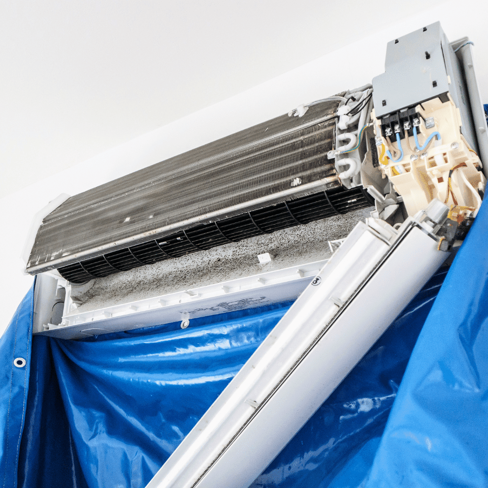 A close-up of an open wall-mounted air conditioner being cleaned for ac replacement, with a blue protective cover catching dust and debris, revealing the internal components and coils.