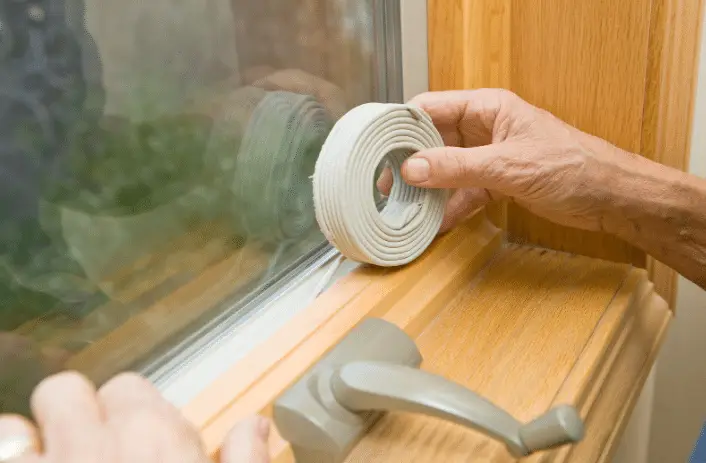 A person applies a rolled weatherstripping tape to the edge of a window frame to insulate, seal gaps, and enhance pest-proofing.