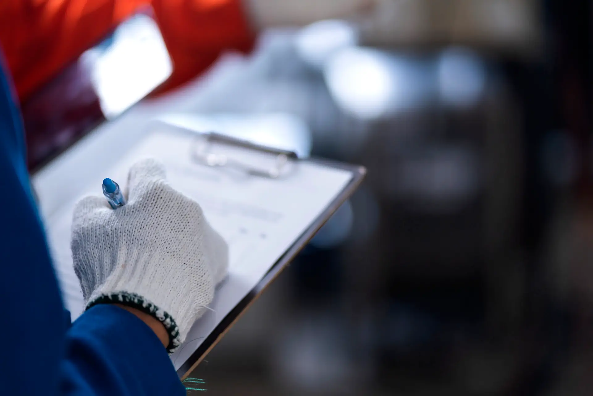 A person wearing a white glove writes on a clipboard with a pen, holding the board in one hand—capturing the precision required during commercial building inspections.