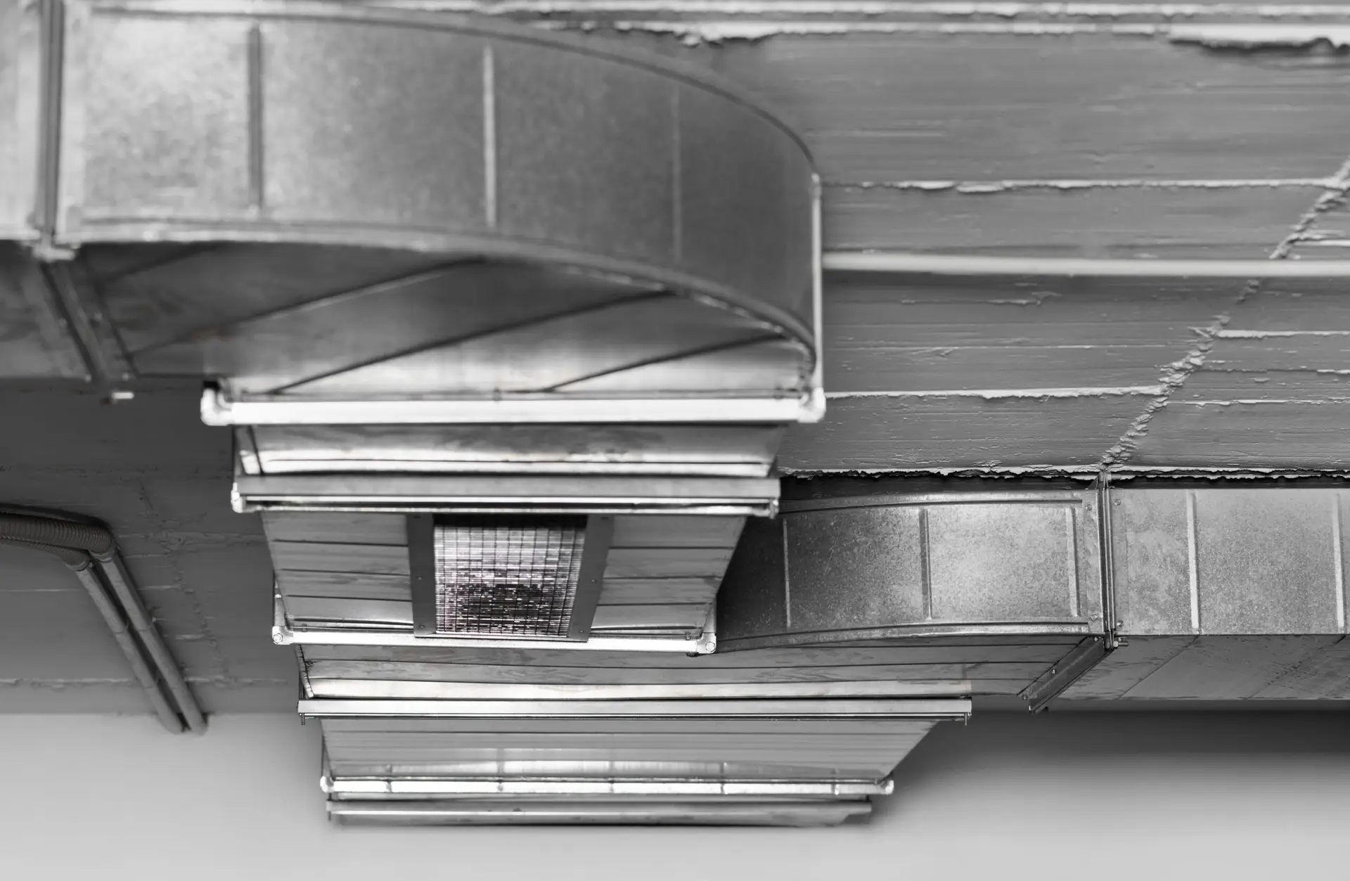Close-up view of metal air ducts and vents attached to a ceiling, featuring industrial-style exposed ductwork inspected by a Dallas home inspector and a light fixture in a grayscale color scheme.