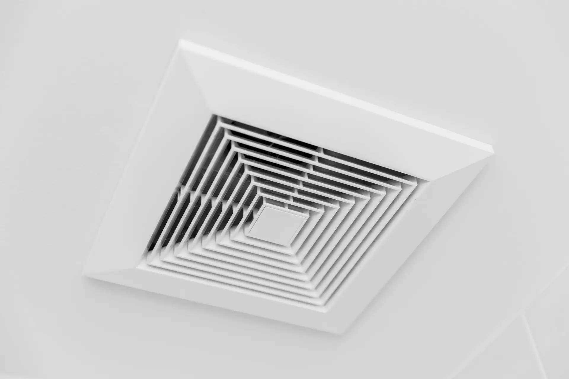 A close-up view of a white ceiling vent with a geometric, square-patterned grill, highlighting where duct cleaning services are often performed on smooth ceiling surfaces.