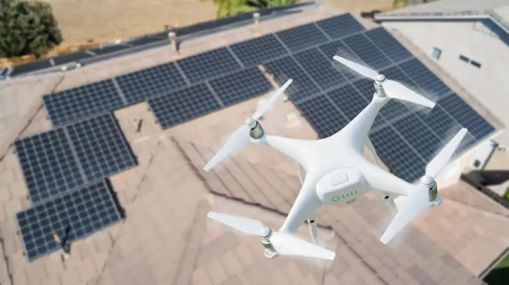 A white drone flies above a rooftop covered with solar panels, capturing an aerial view that highlights the difference between home inspection and appraisal for solar energy installations on a sunny day.