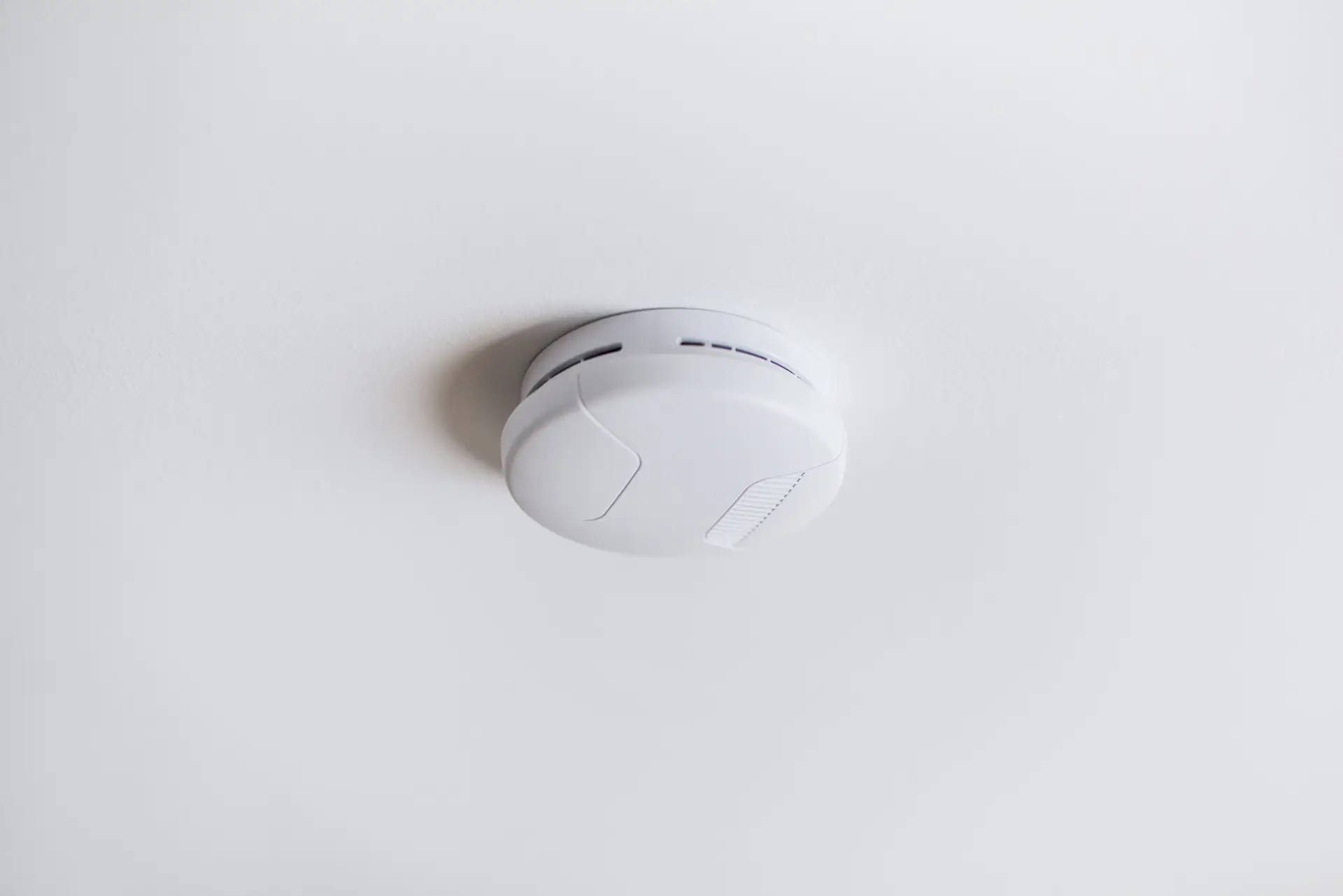 A white smoke detector mounted on a smooth white ceiling, photographed from below during a Dallas home inspector’s evaluation.