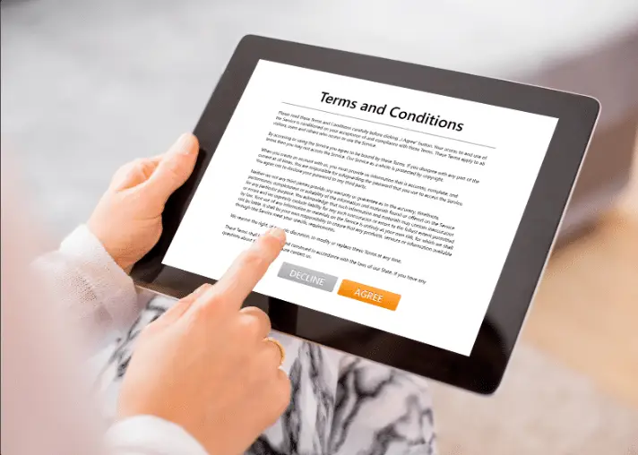 A person holds a tablet, tapping “AGREE” on a Terms and Conditions screen—only their hands and part of their lap are visible, highlighting the importance of client data protection in the real estate industry.