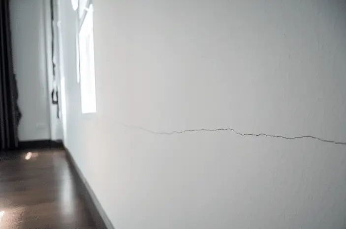 A long, thin crack runs horizontally across a white wall in a room with wooden flooring and natural light, indicating the need for foundation repair near me.